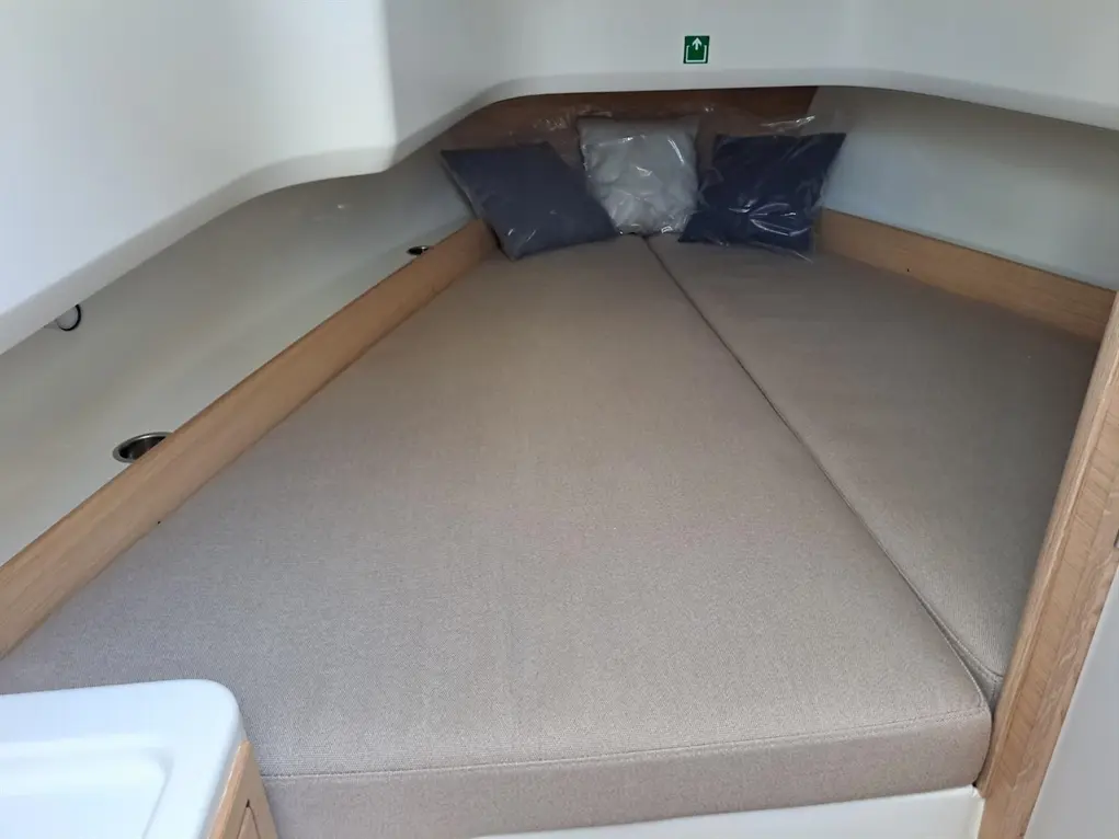 Cozy boat cabin featuring a double bed with beige cushions and decorative pillows in shades of blue and grey against wooden panels.
